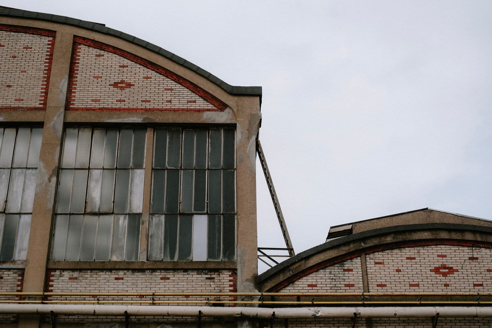Close-up of a red brick factory building with large, weathered windows under a cloudy sky.