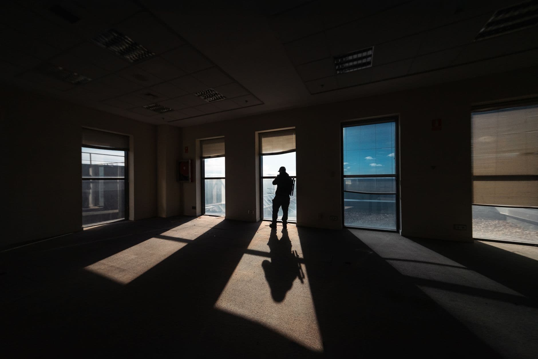 A lone figure casts a shadow in a brightly lit room with large windows.